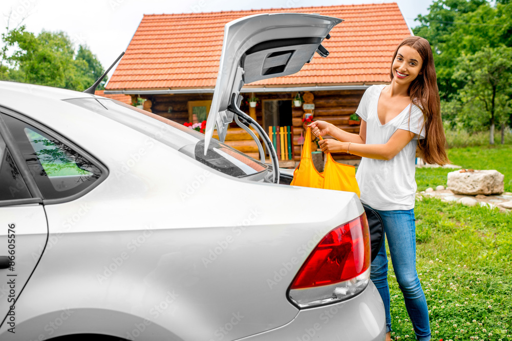 Woman packing near the car with house on backgraound