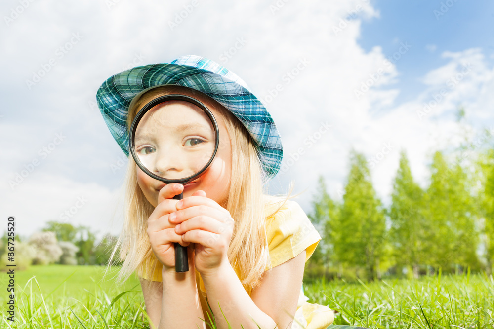Beautiful girl with magnifier laying on the grass