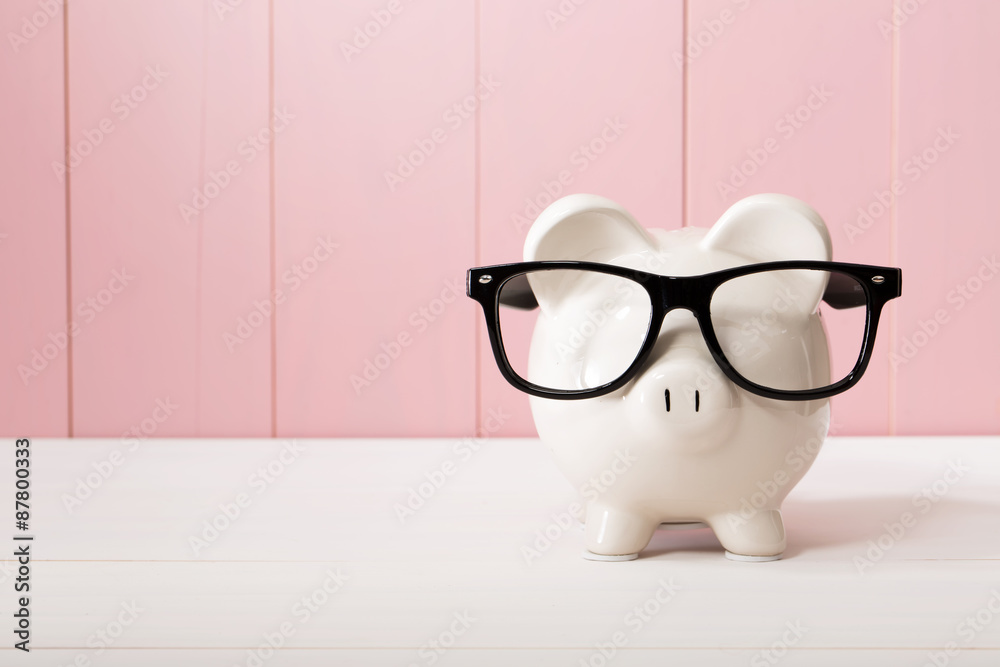 Piggy bank with glasses over pink wooden wall