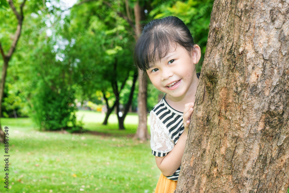 公园里树后微笑的亚洲小女孩