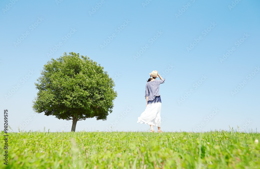 一本木のある原っぱに立つ女性