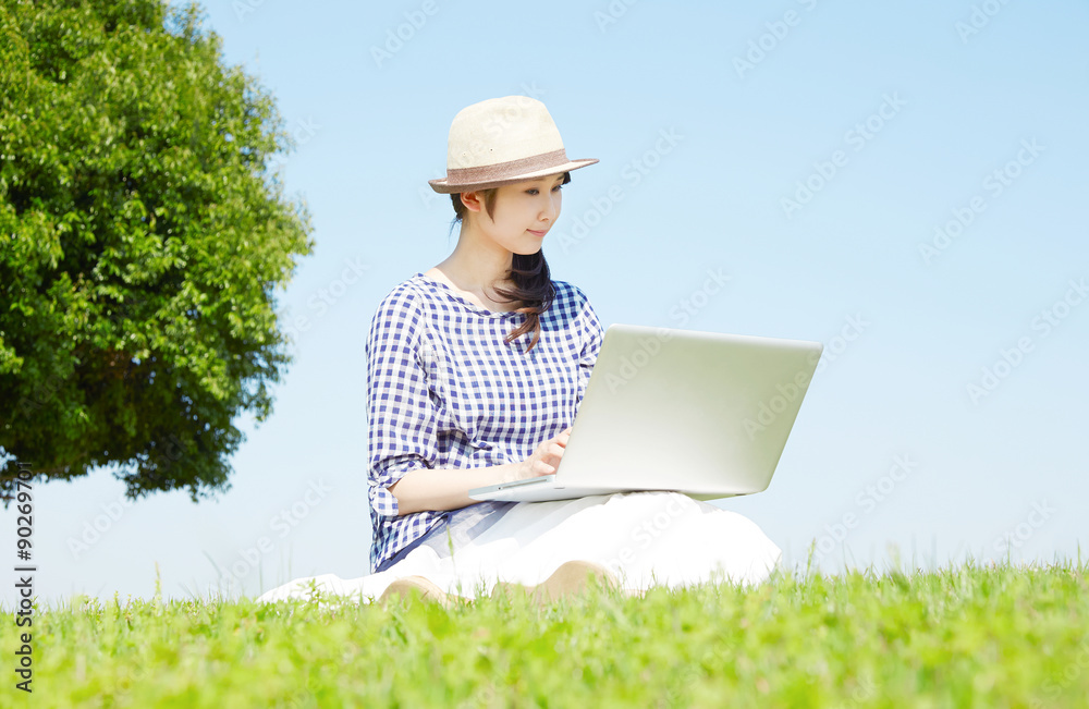 原っぱでノートパソコンを使う女性