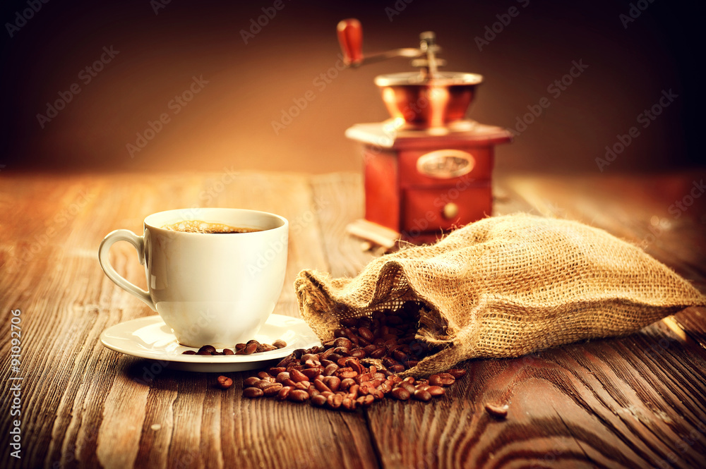 一杯咖啡，木桌上放满了烤咖啡豆和咖啡磨