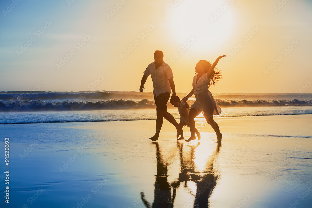 幸福的家庭——爸爸、妈妈、宝贝儿子牵着手，在布拉克岛的日落海边快乐地奔跑