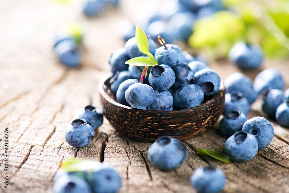 Juicy and fresh blueberries with green leaves in wooden bowl