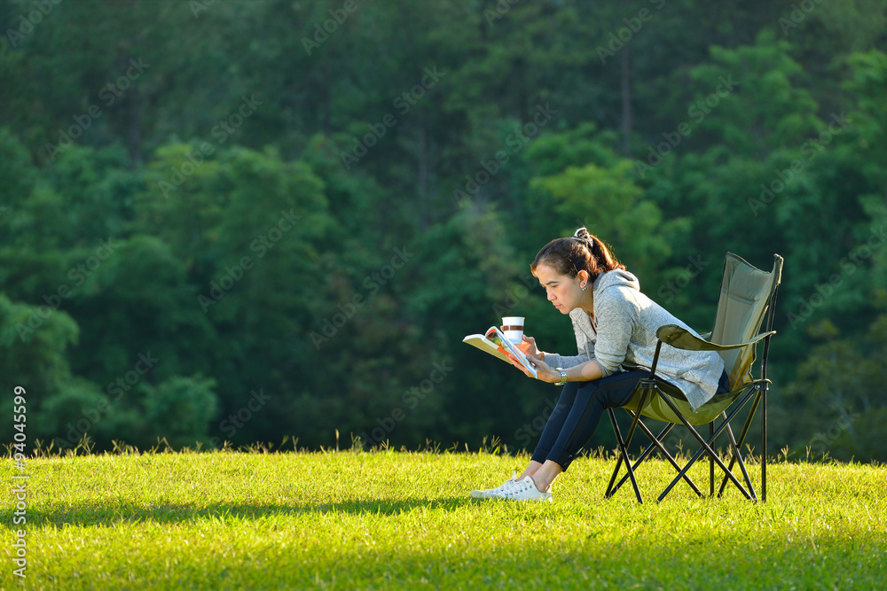 年轻女子坐在公园里看书，手里拿着纸咖啡杯