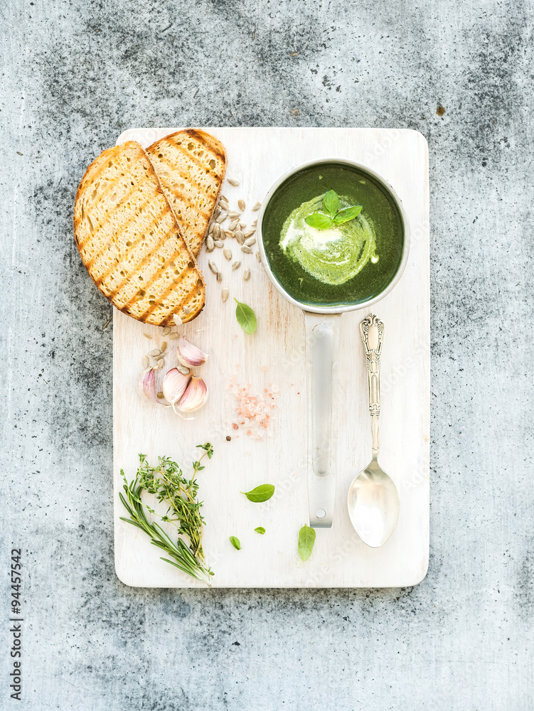 自制绿色菠菜奶油汤，放在金属勺中，配烤面包片、香草和白色香料