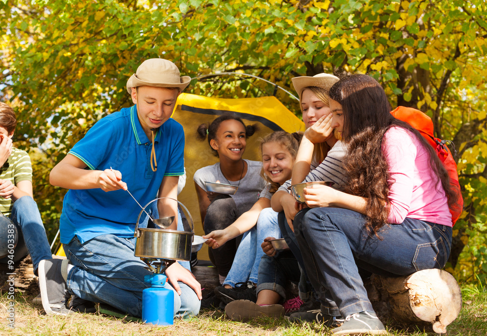 Boy cooking soup in pot for friends at  campsite