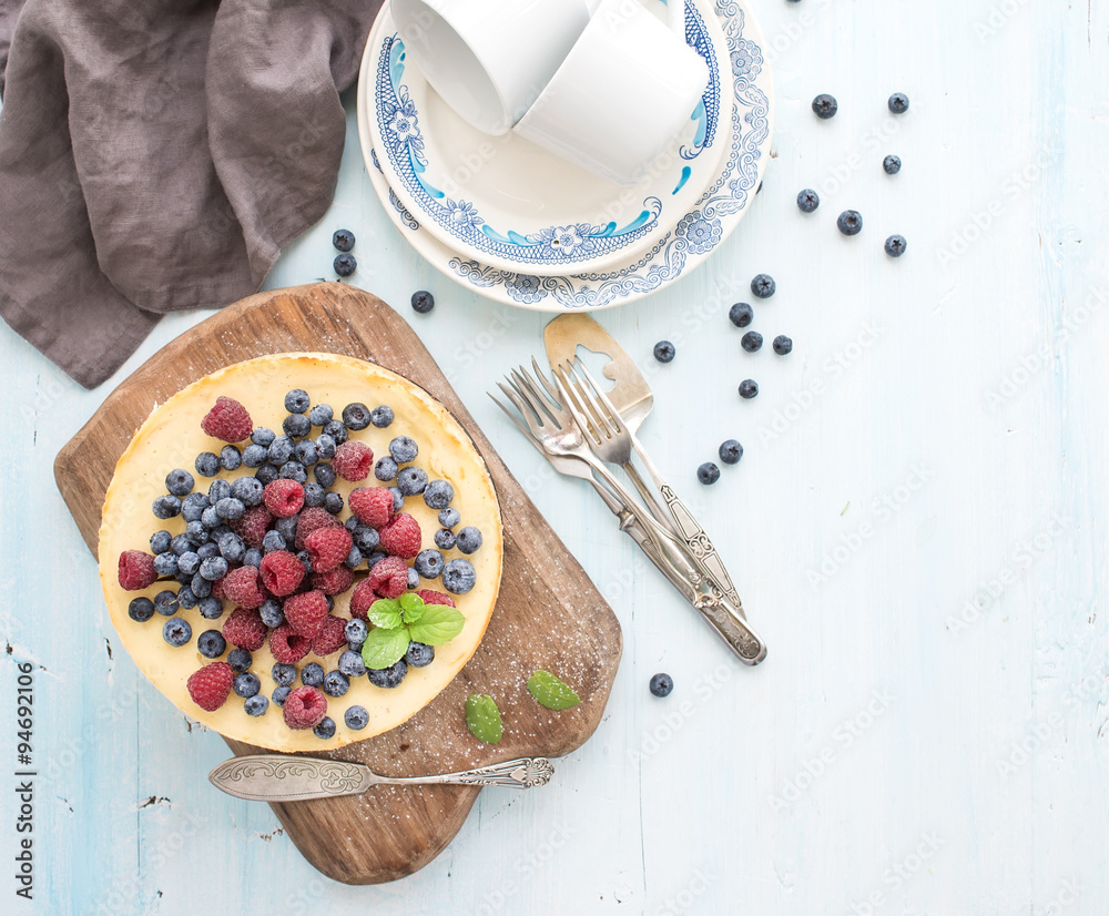 用新鲜树莓和蓝莓做成的奶酪蛋糕，放在木制的服务板、盘子、杯子、厨房n上