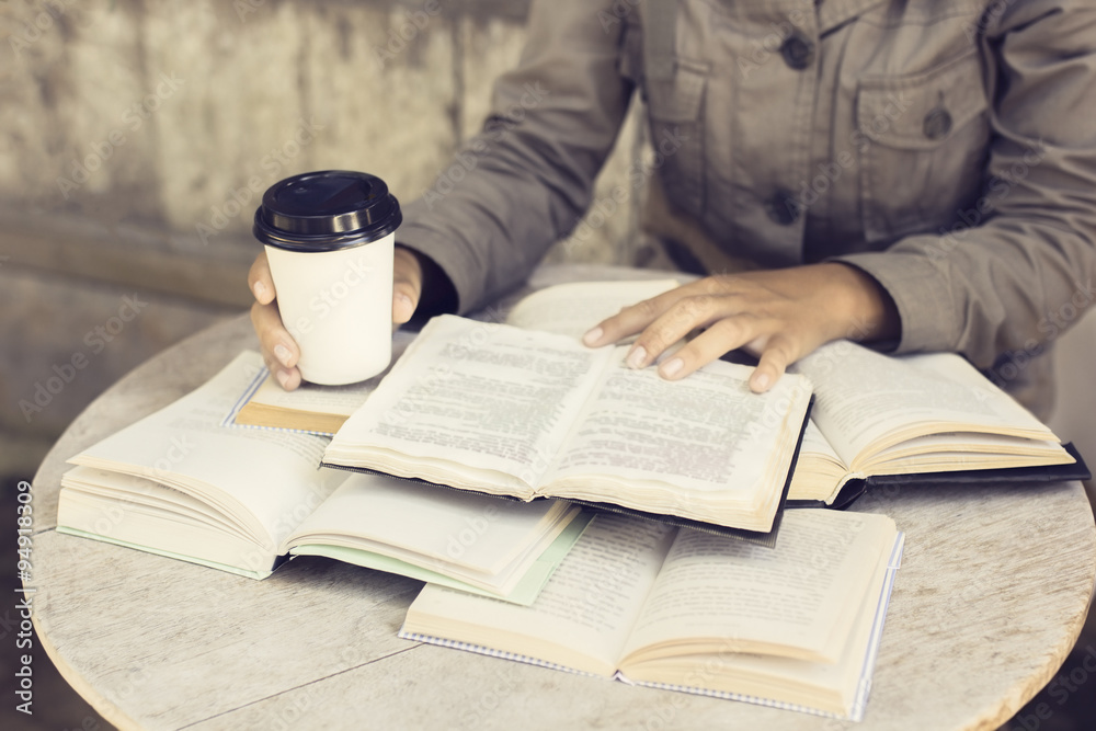 Girl with coffee to go and many open books on wooden table