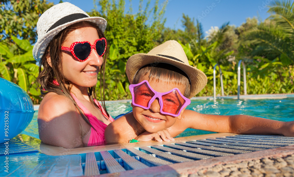 快乐的女人和她的儿子在游泳池里戴着墨镜