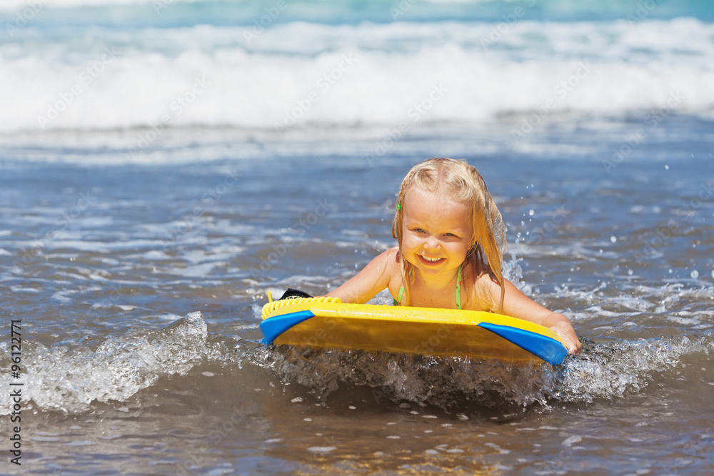 小女婴-带着冲浪板的年轻冲浪者在小海浪上玩得很开心。积极的家庭生活方式