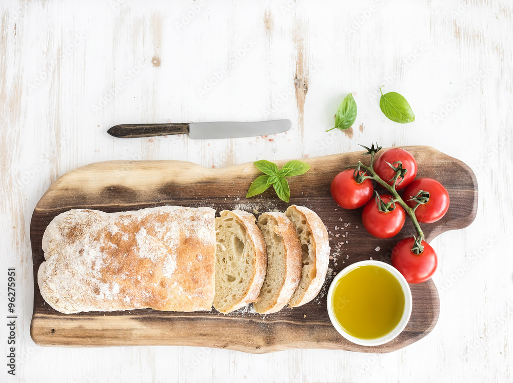 新鲜烘焙的ciabatta面包，核桃木板上有樱桃番茄、橄榄油、罗勒和盐