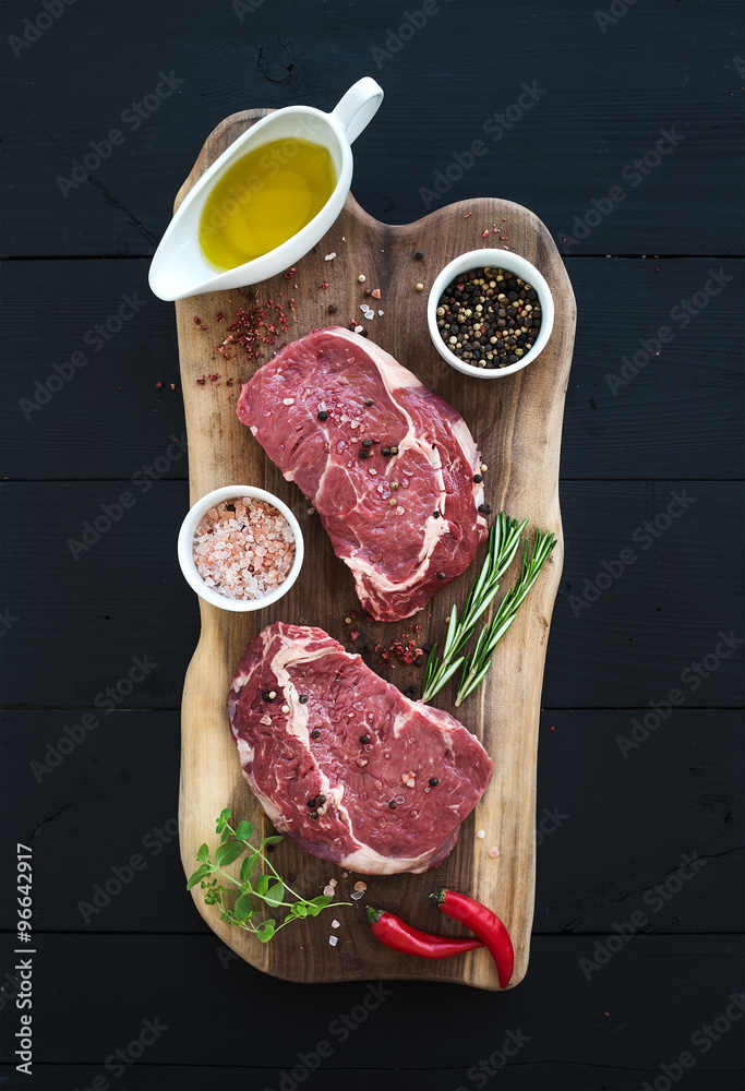 深色木质背景下的生鲜肉肋眼牛排主菜和砧板上的调味料