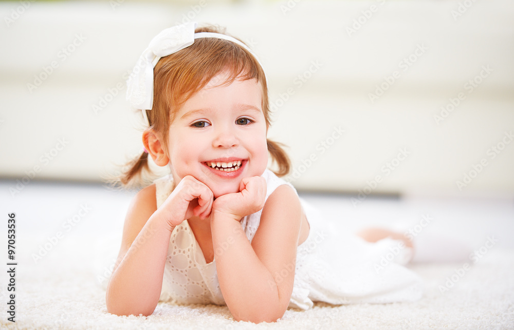 Happy little girl lying on floor in a white room