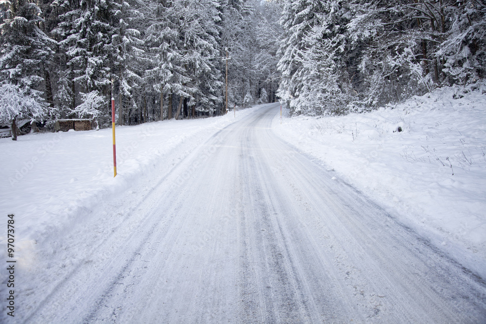 大雪纷飞的乡村道路。泥泞的雪地和结冰的冬季森林犁过道路背景。