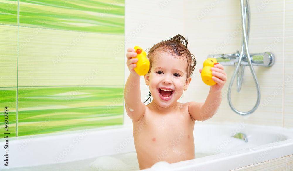 带着黄色鸭子玩具的快乐孩子在泡沫浴缸里洗澡