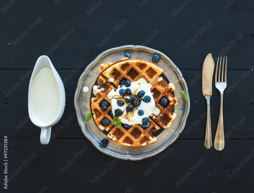 软比利时华夫饼，配蓝莓、蜂蜜和鲜奶油，放在复古金属盘上，配上黑宇