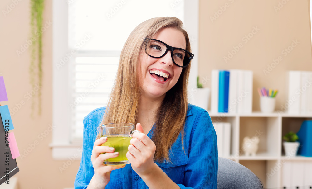 快乐的年轻女人在她的家庭办公室喝茶