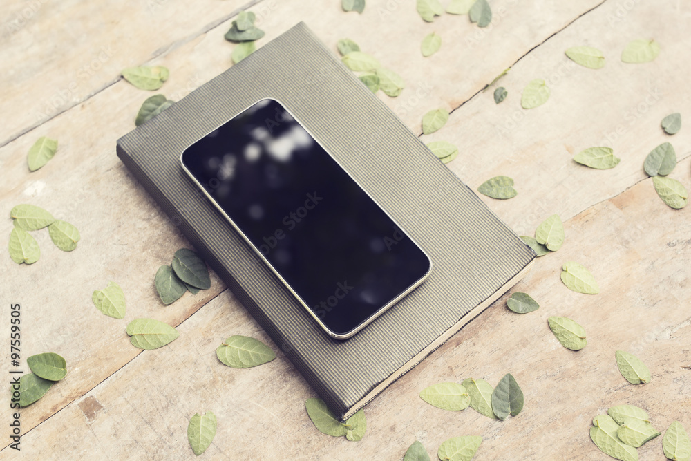 日记本上的空白黑色智能手机屏幕，木质标签上有树叶