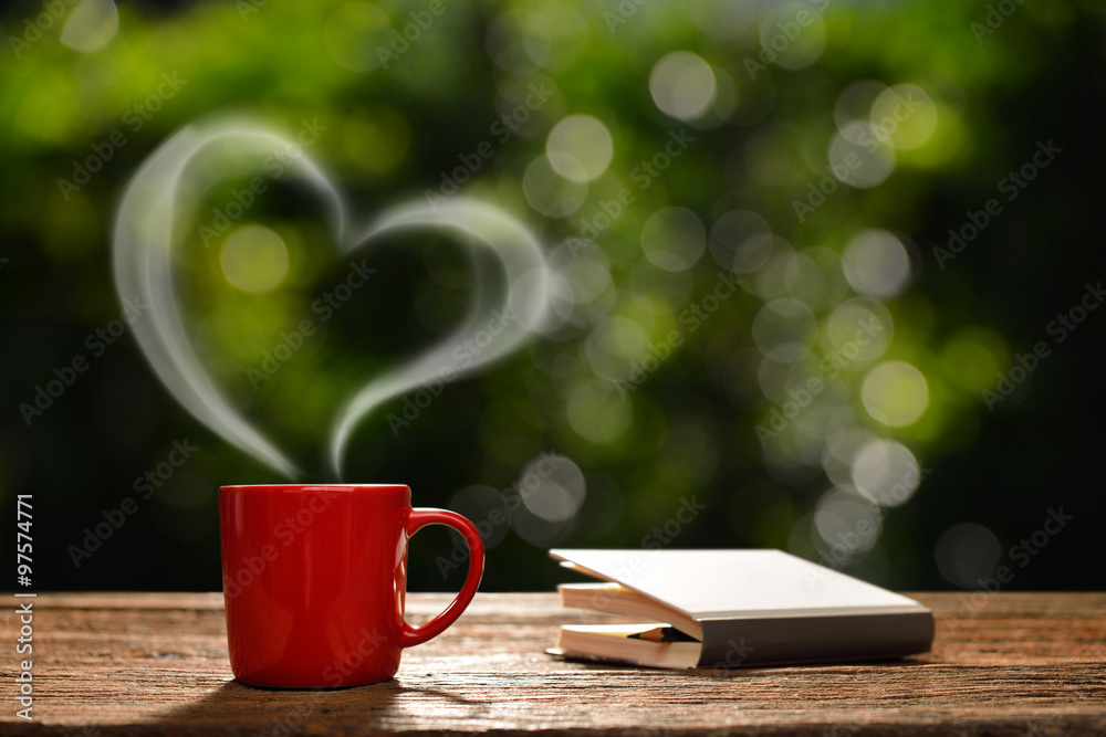 Cup of coffee with heart-shaped smoke and book in the garden