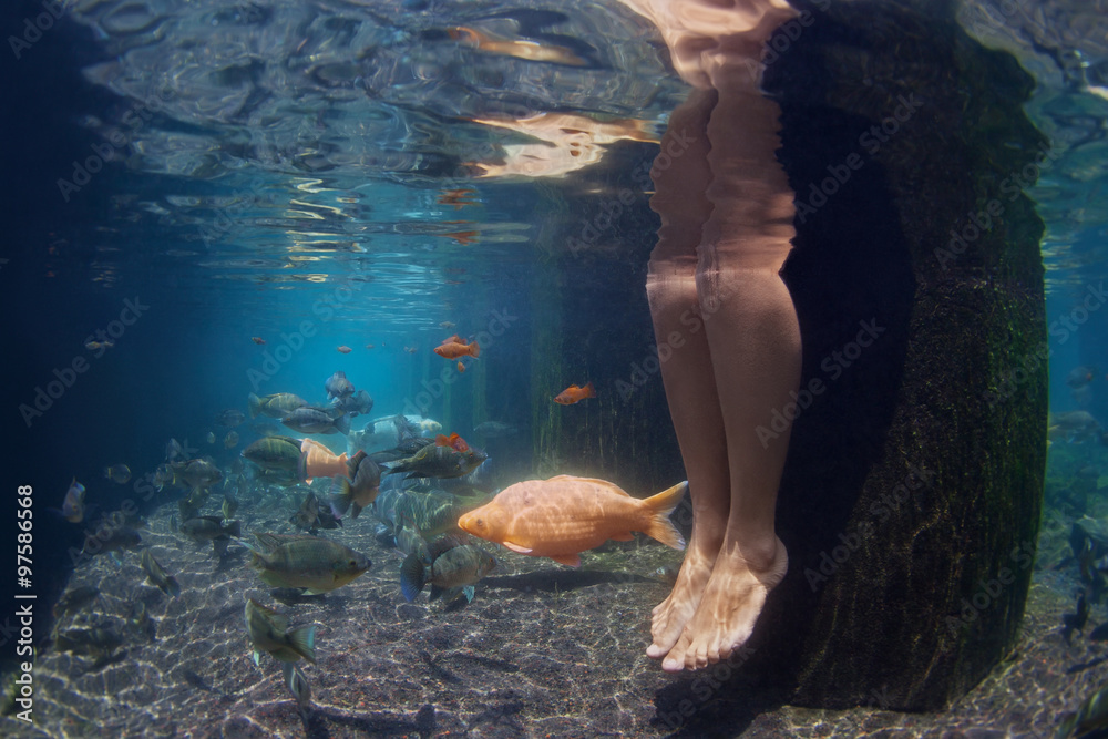 年轻女子的腿在水疗池放松的水下照片，金鱼在淡水中游泳