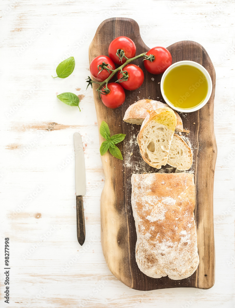 新鲜出炉的ciabatta面包，配樱桃番茄、橄榄油、罗勒和盐，配核桃木板