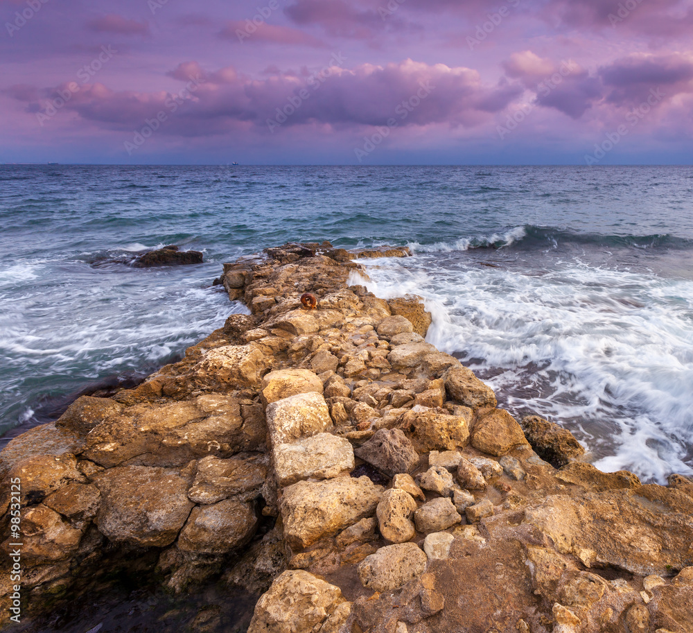 Sea waves with rocks on the beach at sunset