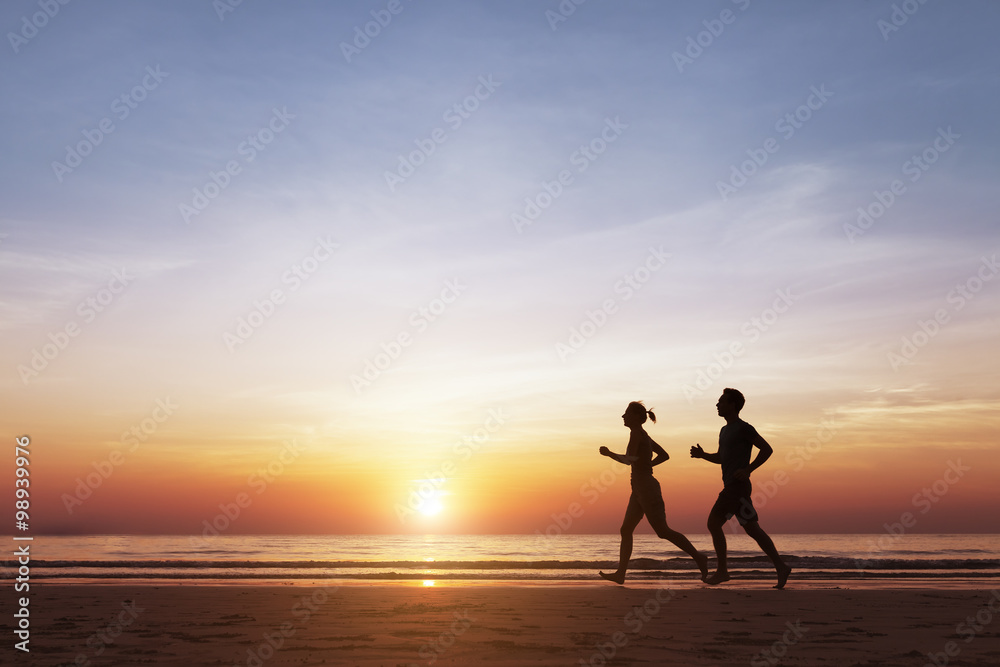 日落时两名跑步者在海滩上跑步的剪影
