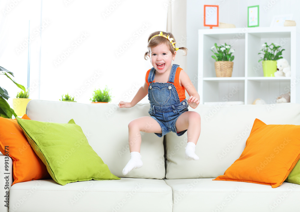 快乐的小女孩在家里的沙发上玩耍和跳跃