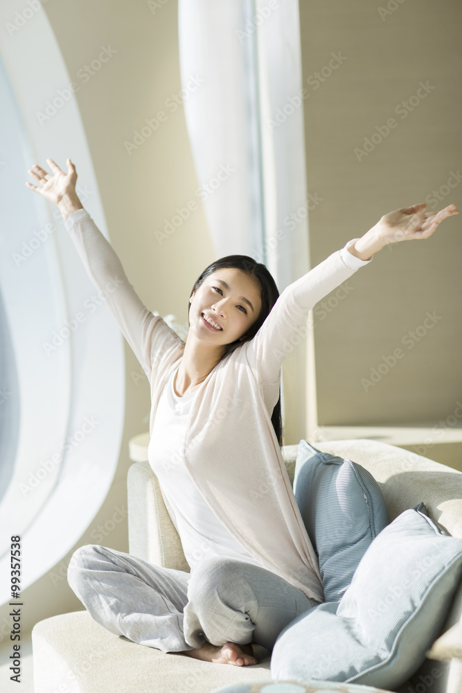 快乐的年轻女人在沙发上伸展双臂