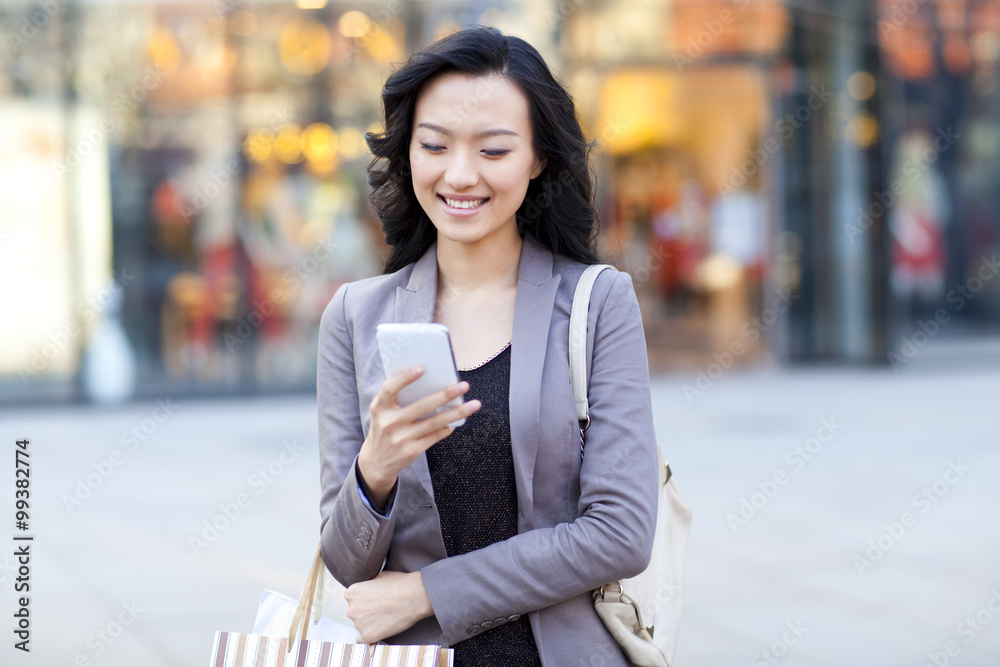 快乐的年轻女人拿着购物袋检查智能手机