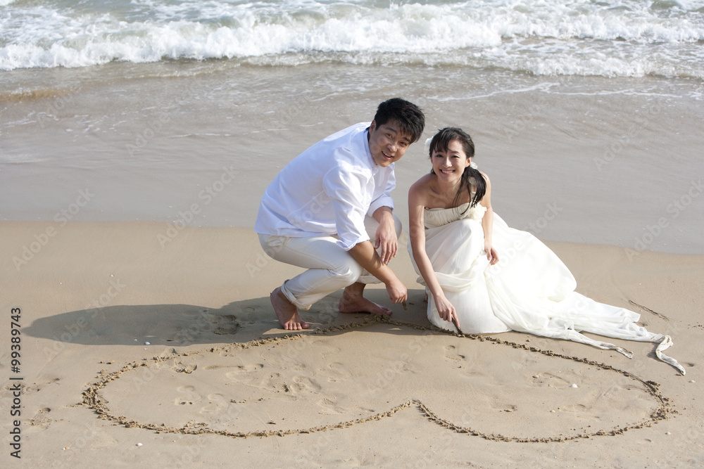 幸福的新婚夫妇在海滩上画心形