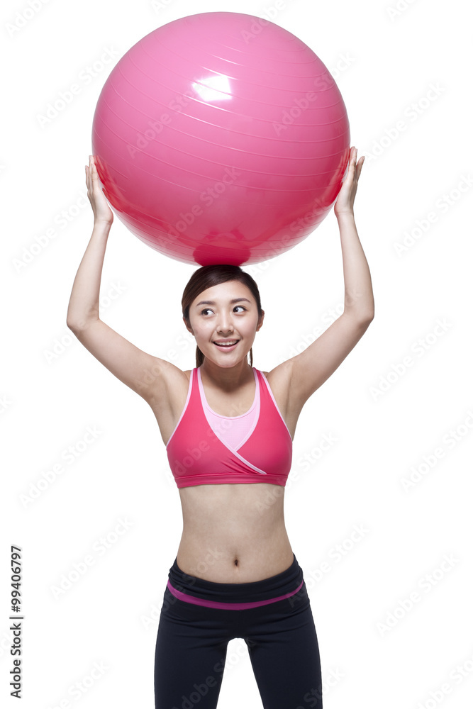 Young woman in sports clothing with a fitness ball on her head