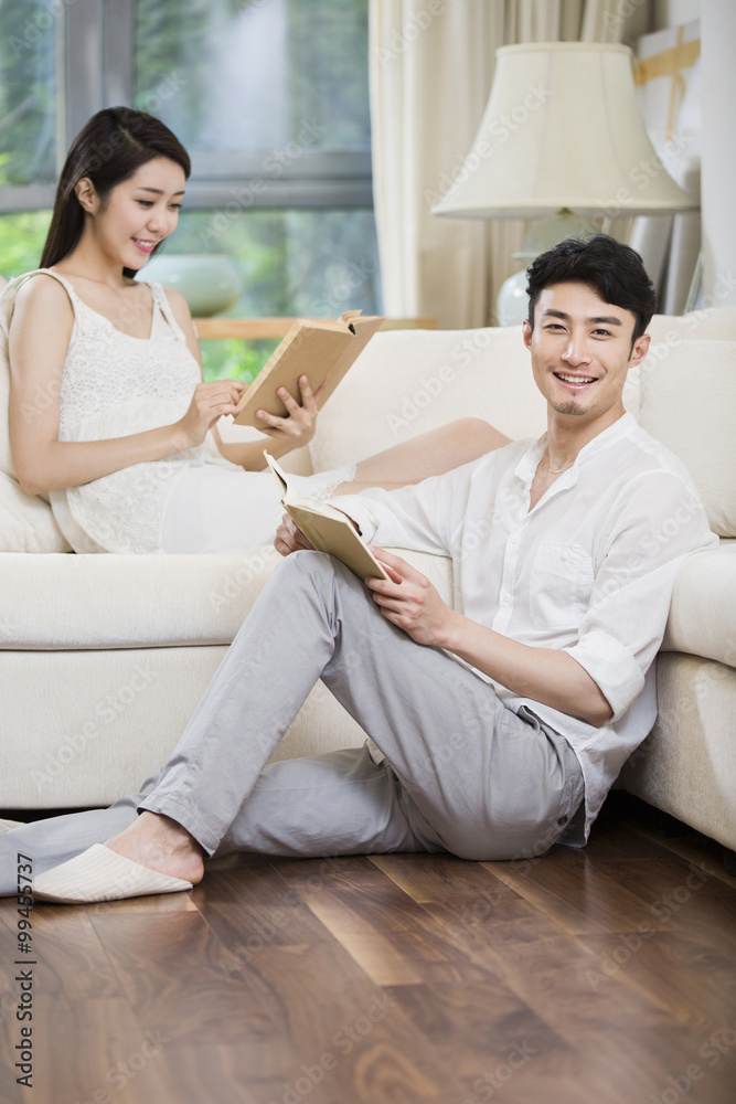 Cheerful young couple reading book in living room
