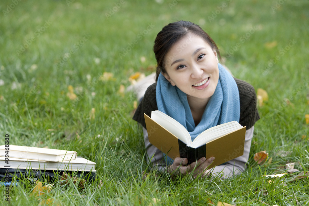 A young woman reading books while lying on grass