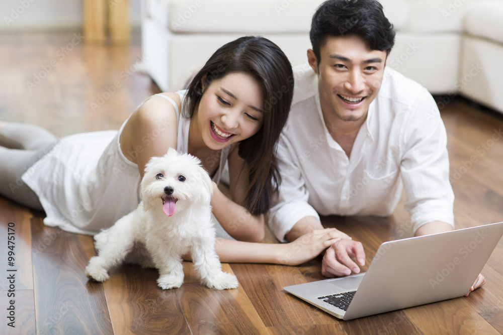 Young couple lying on floor using laptop with a cute dog