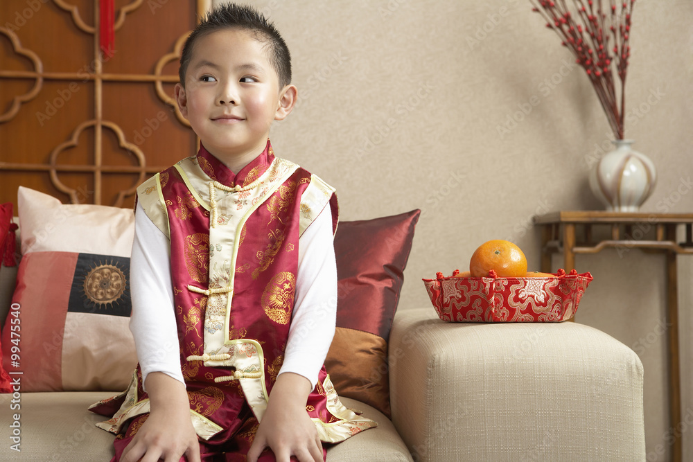 穿着传统服装坐在沙发上的小男孩看起来很调皮