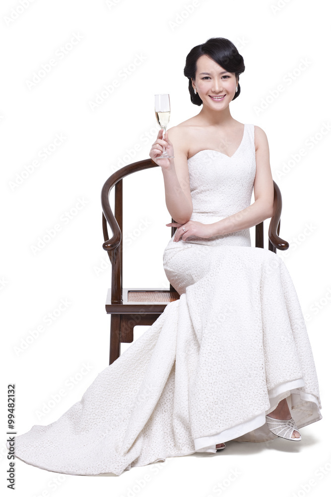 优雅的年轻女子坐在中国明代木扶手椅上，手里拿着香槟长笛
