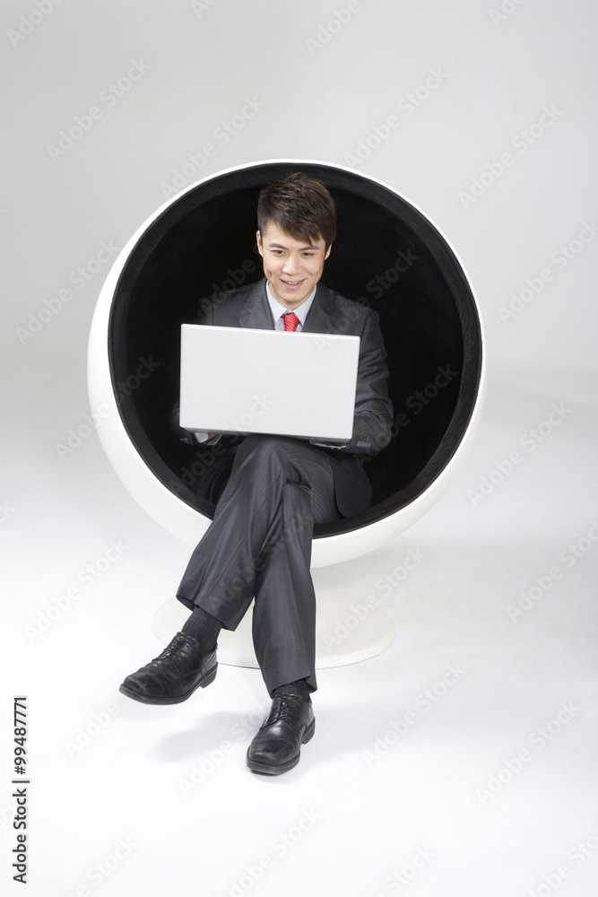 年轻商人在球椅上使用笔记本电脑