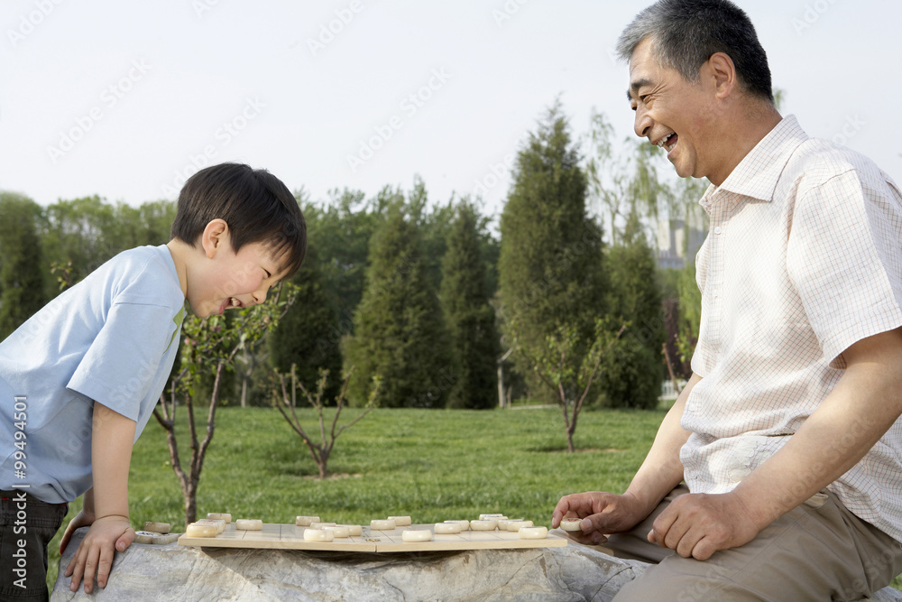 Grandfather And Grandson Playing A Boardgame In The Park