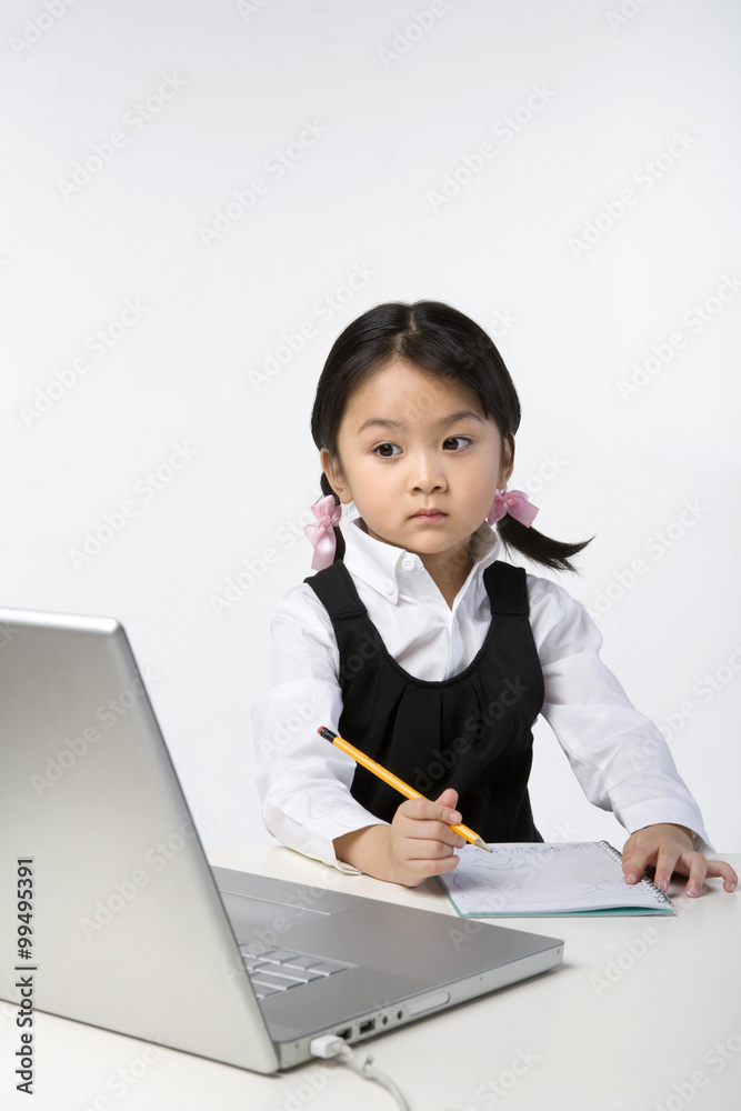 Little girl uses a laptop and a notebook