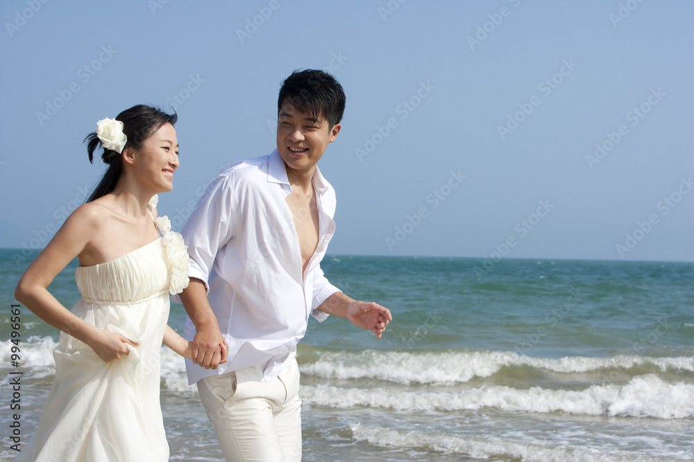 幸福的新婚夫妇在海滩上奔跑