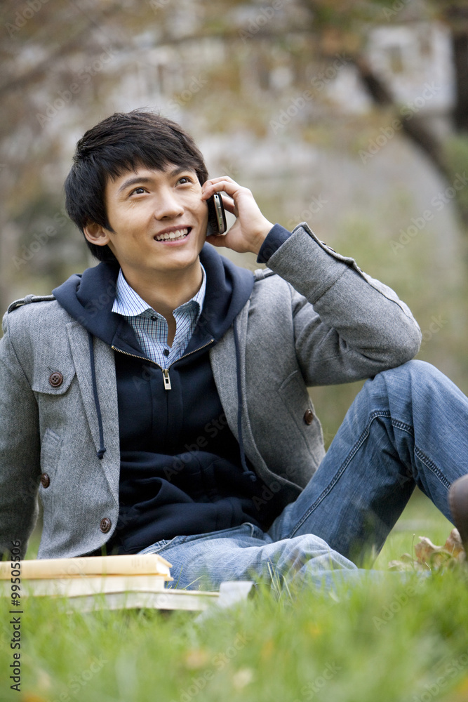一个年轻人坐在草地上打电话