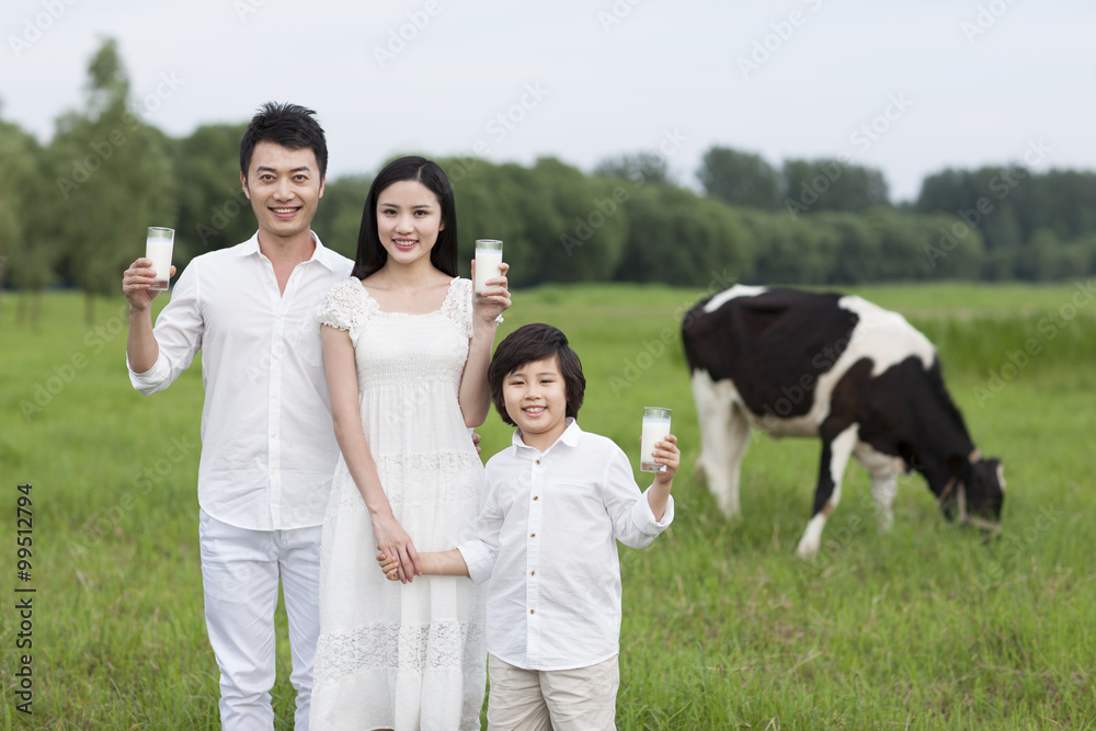 幸福的一家人拿着一杯牛奶，牛群在牧场上吃草