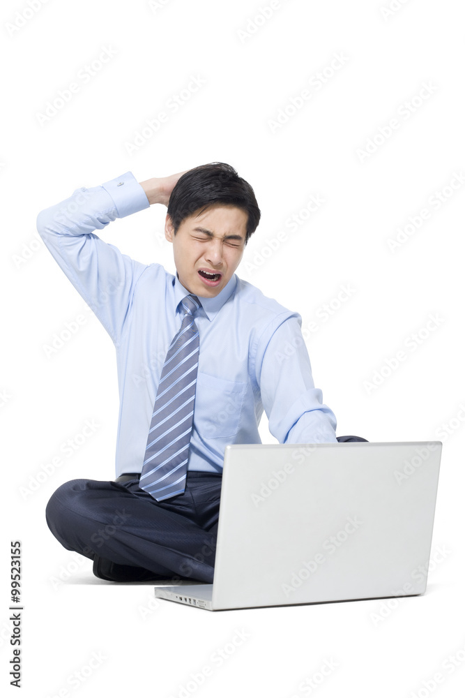 一个沮丧的商人拿着笔记本电脑坐在地板上