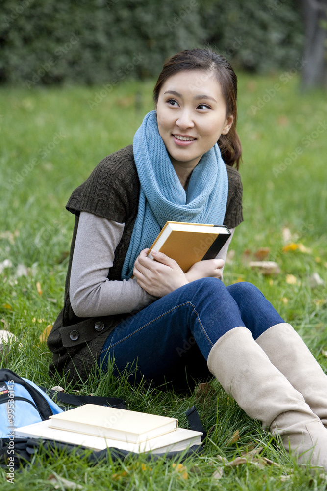 一名年轻女子坐在草地上拿着一本书