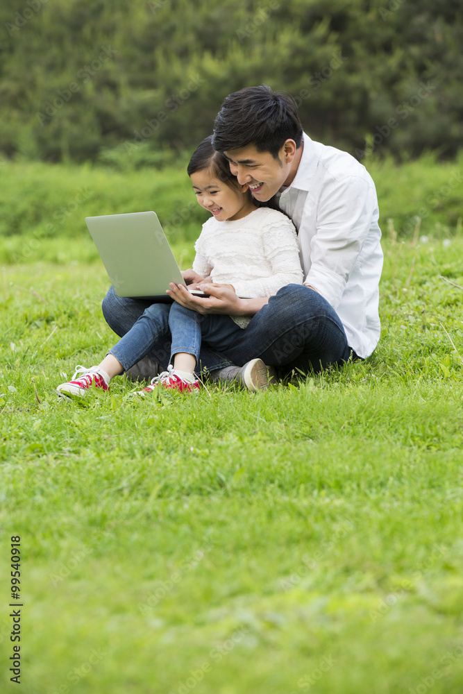 父女在草地上使用笔记本电脑