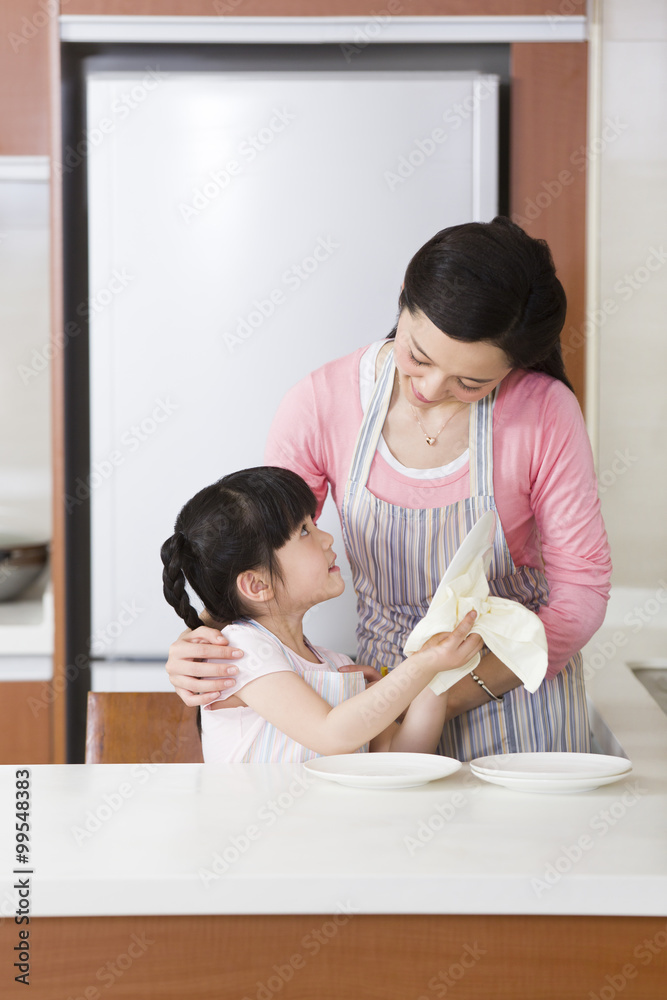 Cute girl drying plates for her mother