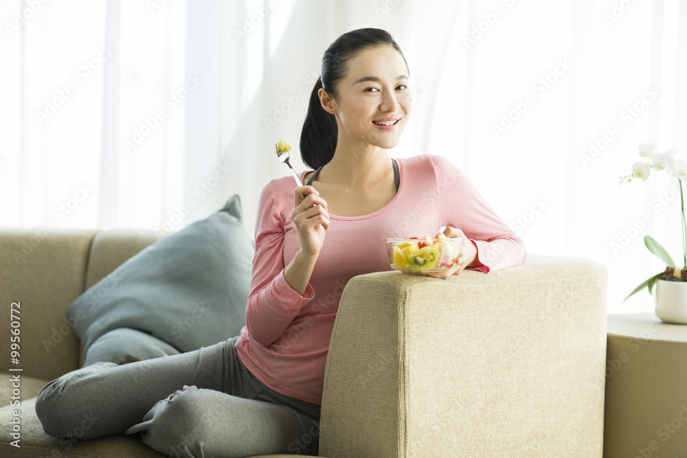 Happy young woman eating fruit salad